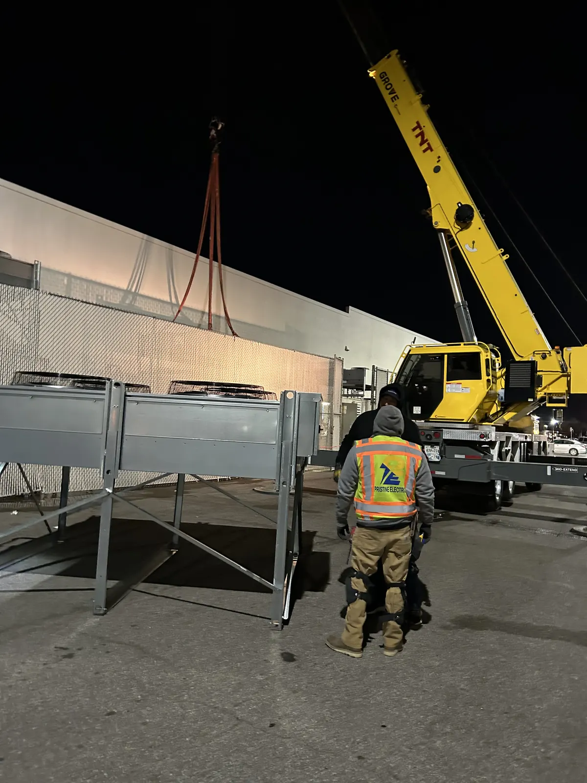 Crane setting rooftop HVAC equipment while a Pristine Electric electrician watches